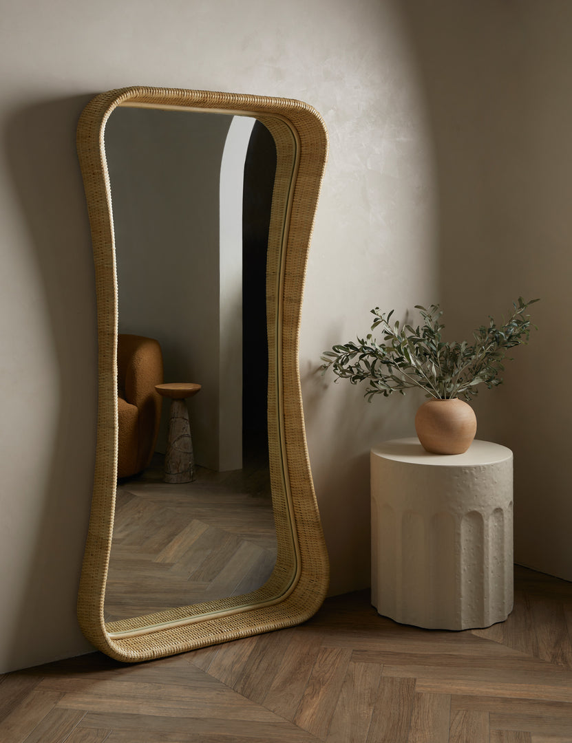 #color::natural | Howell wicker frame floor mirror leaning against a wall next to a round side table with a decorative vase.