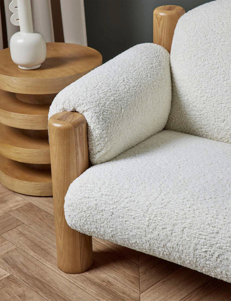 | The James faux sherpa accent chair sits atop a chevron hardwood floor next to a four-tiered wooden side table 