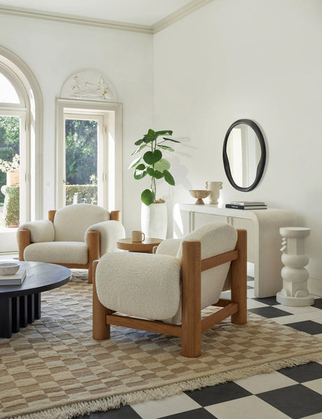 | Two James faux sherpa accent chairs sit atop a natural and ivory checkerboard rug in a room with high ceilings and white walls