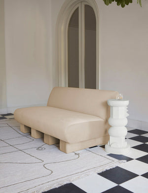 The toivo short pedestal stands next to a beige velvet sofa on top of a checkerboard floor