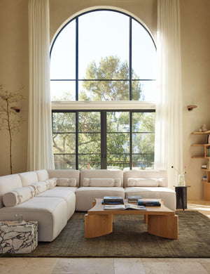 The Chiltern moss rug lays in a bright living room under a white sectional sofa and a square coffee table