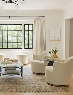 An ivory sofa sits across from two natural boucle Margie rounded swivel chairs atop an orange Arches area rug.