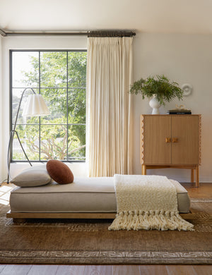 Enola minimalist low daybed styled with a modern floor lamp, fringe throw blanket and round velvet pillow.