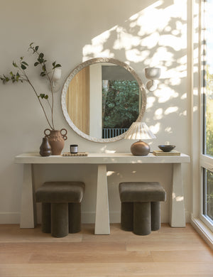 A round wall mirror hangs above the Avila modern narrow console table.