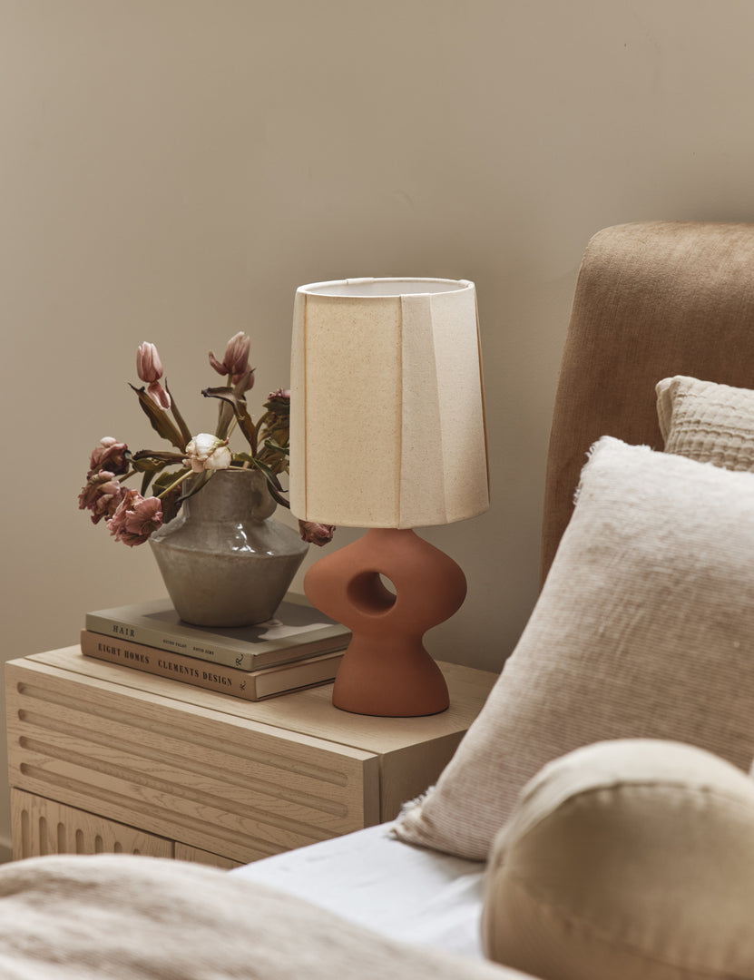 #color::terracotta | Rhodes sculptural ceramic table lamp styled on a nightstand in a bedroom.
