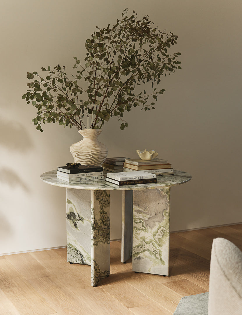#color::green-onyx-marble | Celia round dining table styled with various books and a large sculptural vase filled with botanicals.
