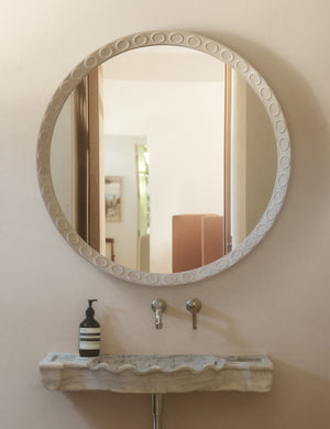 Correa round distressed wood frame wall mirror hanging over a bathroom sink.