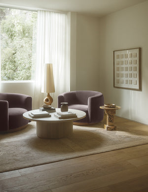 Halden handwoven carved design rug styled with a round stone coffee table and two purple velvet accent chairs.