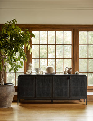 The Brooke black solid oak sideboard sits in a room with wooden framed windows with decorative objects sitting atop it