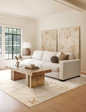 The evet rug lays in a living room with two large floral wall arts under a burl wood coffee table and an ivory linen sofa
