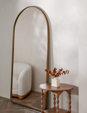 Idris thin metal framed floor length mirror in gold styled next to a side table and accent chair