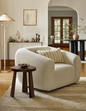 Harlowe softly sculpted plush swivel accent chair styled with a round side table, striped linen lumbar pillow and textured rug.