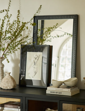 Thelma black carved wood framed mirror styled with a framed print and ceramic vases on top of a black console cabinet