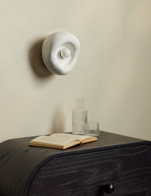 Odette round matte white sculptural wall sconce above a black nighstand