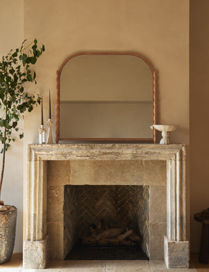 Topia arched carved wood mantel mirror by Ginny Macdonald in natural hung above a fireplace.