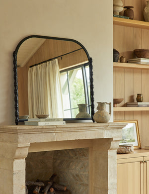 Topia arched carved wood mantel mirror by Ginny Macdonald in black styled above a fireplace.