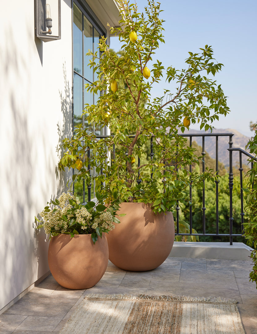 #size::medium #size::small | Kenna small and medium rounded fiberstone planters with plants outside on a porch.