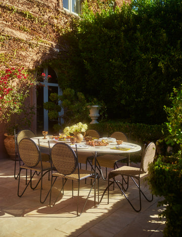 #color::faux-travertine | Outdoor patio dining space featuring the Peggy sculptural iron frame and stone top oval outdoor dining table.