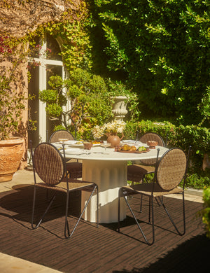Four Ziggy modern wicker outdoor dining chair by Sarah Sherman Samuel placed around a white round outdoor dining table.