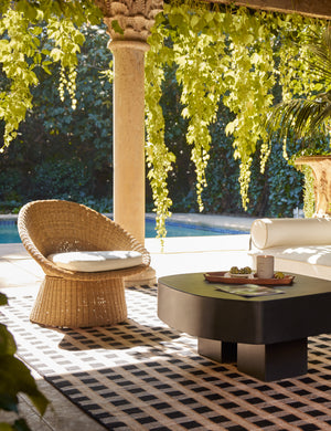 Ferran sculptural wicker outdoor accent chair styled with a black outdoor coffee table and black outdoor rug.