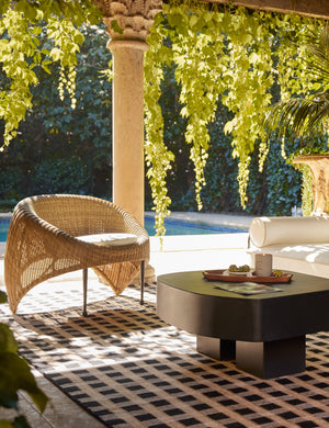 Marisol sculptural wicker outdoor accent chair styled with a black outdoor coffee table and black and tan outdoor rug.