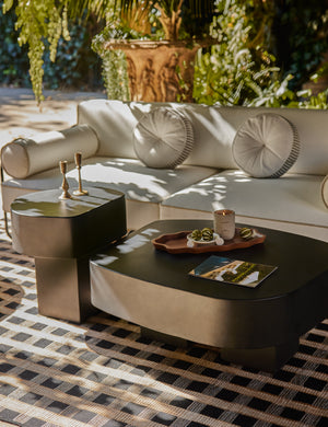 The Armas black monolithic round outdoor coffee table by Sarah Sherman Samuel is styled with a white modern outdoor sofa and black and tan basketweave design outdoor rug.