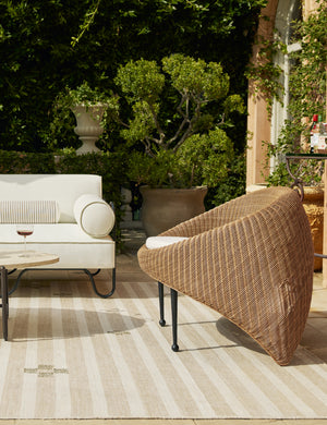 Marisol sculptural wicker outdoor accent chair styled with a modern outdoor sofa and neutral striped outdoor rug.