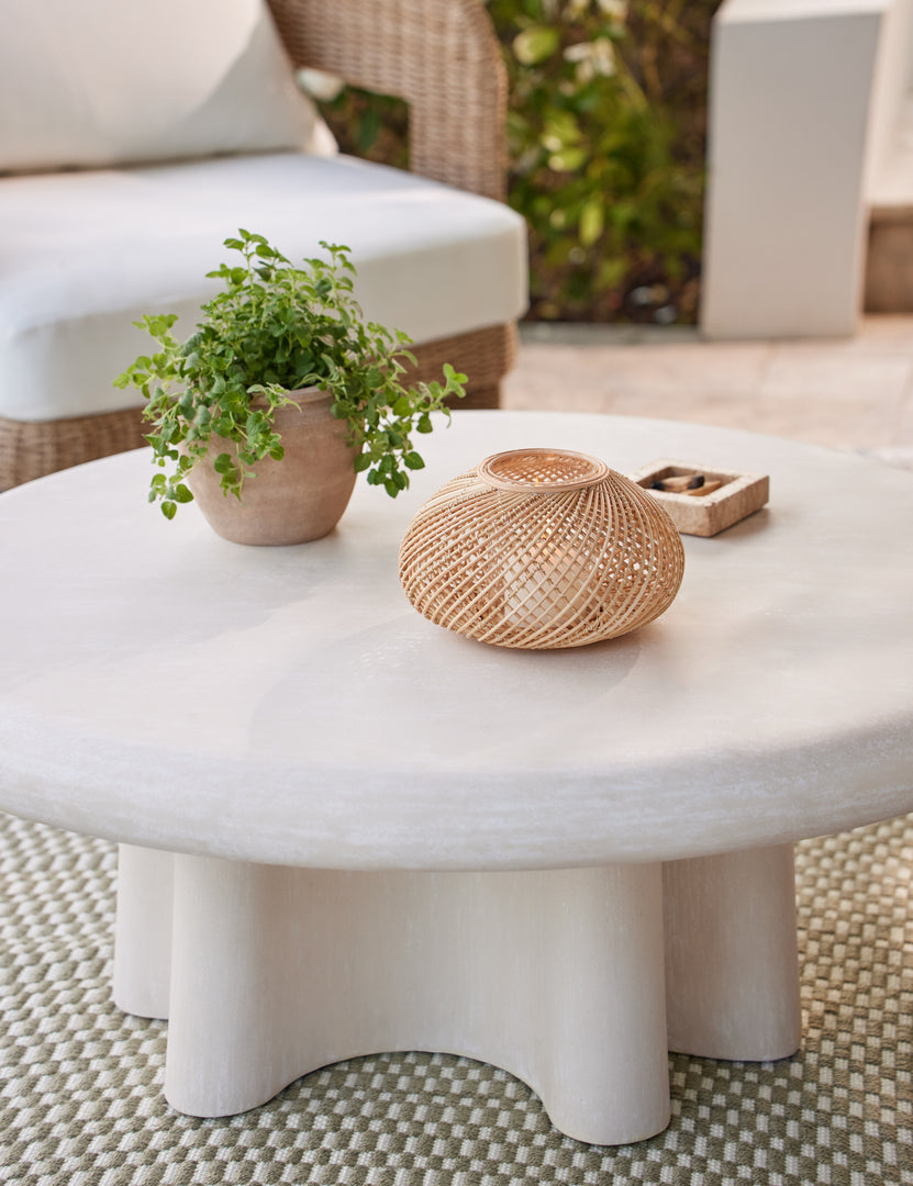 #color::ivory | Ruiz round cement outdoor coffee table styled with a woven lantern candleholder and potted plant.