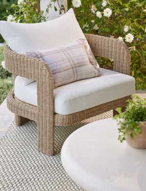 Priya plaid fringed outdoor lumbar pillow styled on a wicker outdoor accent chair.