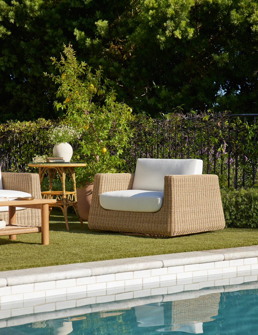 #color::natural | Aisha wide arm modern wicker outdoor swivel chair in a poolside lounge.