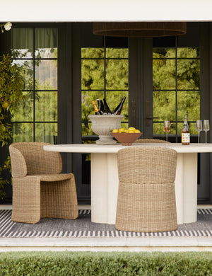 Two Mettam modern wicker outdoor dining chairs styled with a stone oval outdoor dining table.