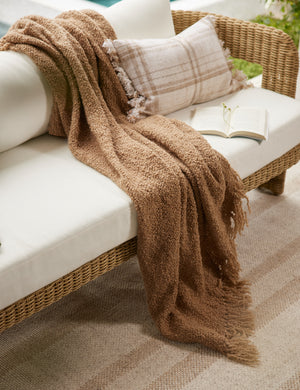 Hadler modern sculptural open frame wicker outdoor sofa with a outdoor throw blanket draped overtop.