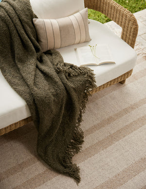 Jaffe chunky knit fringed outdoor throw blanket in moss draped over an outdoor sofa.