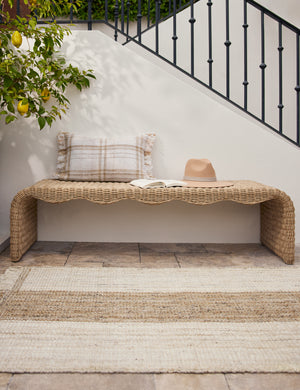 Wicker outdoor bench styled with the Sabriel handwoven large-scale striped fringed outdoor rug.