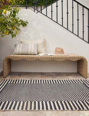 Wicker bench styled with the Lavinia handwoven high contrast outdoor rug.