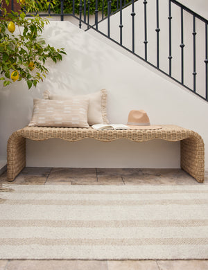 The Croze handwoven striped fringed outdoor rug in front of an outdoor wicker bench.