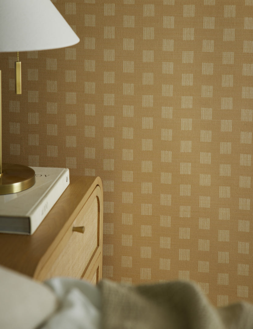 #color::natural | Close up view of the Sand Dune Grasscloth Wallpaper by Élan Byrd on a bedroom wall.