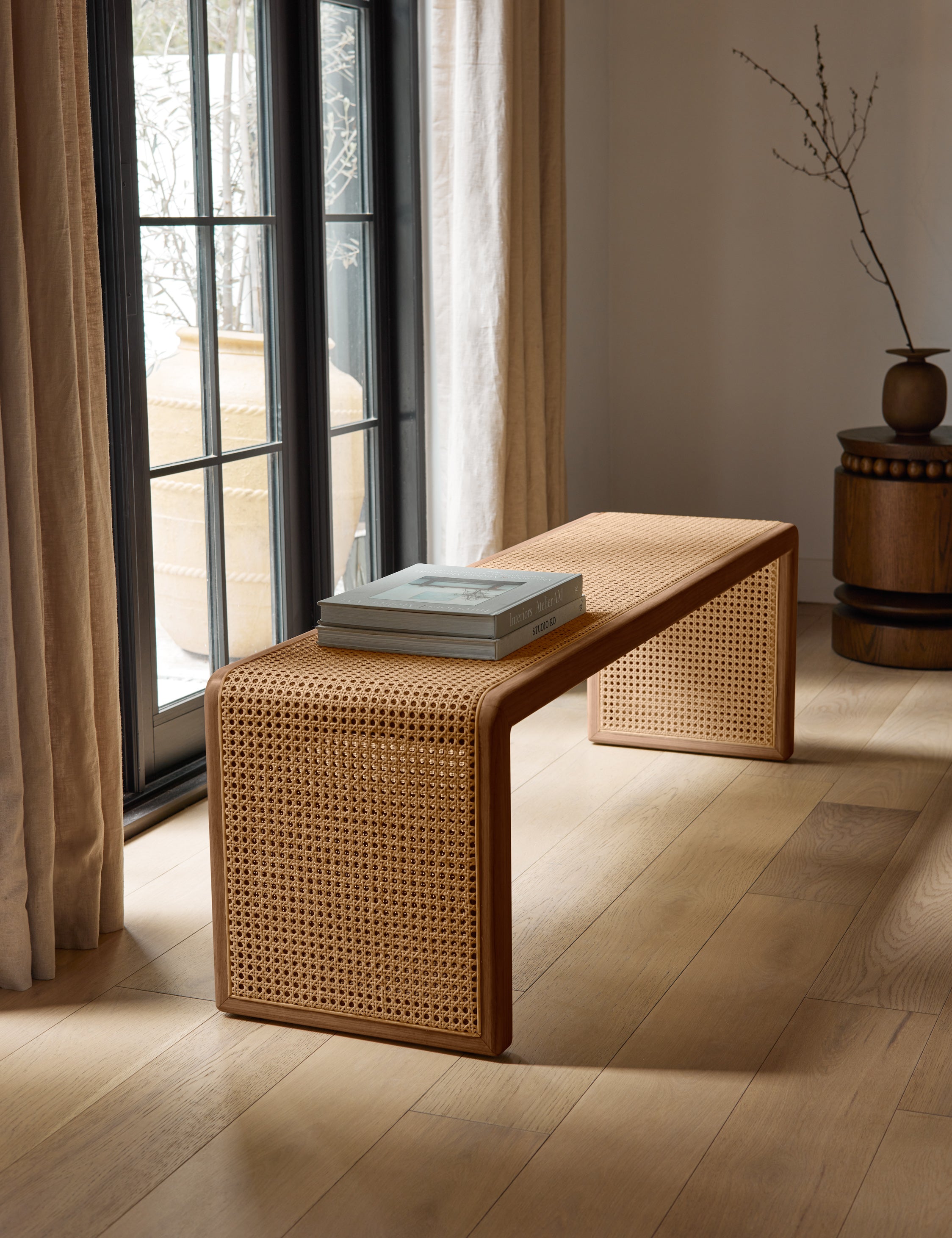 #color::light-espresso | Canistel woven cane waterfall bench by Carly Cushnie styled in front of a large window.