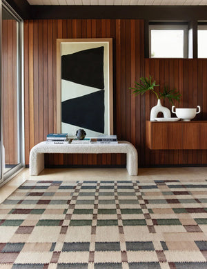 The marli rug lays in a retro room with wood-paneled wall, a geometric wall art, and a cream boucle bench