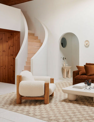 The James faux sherpa accent chair sits atop and natural and ivory rug in front of a natural wooden curved staircase