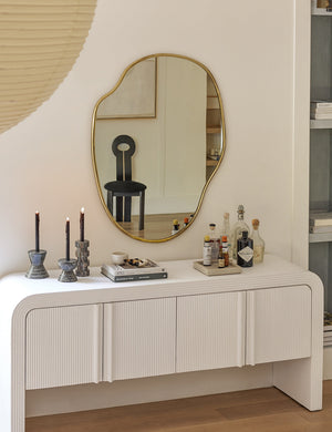 The small puddle mirror reflects a black dining chair and hangs over a textured white sideboard