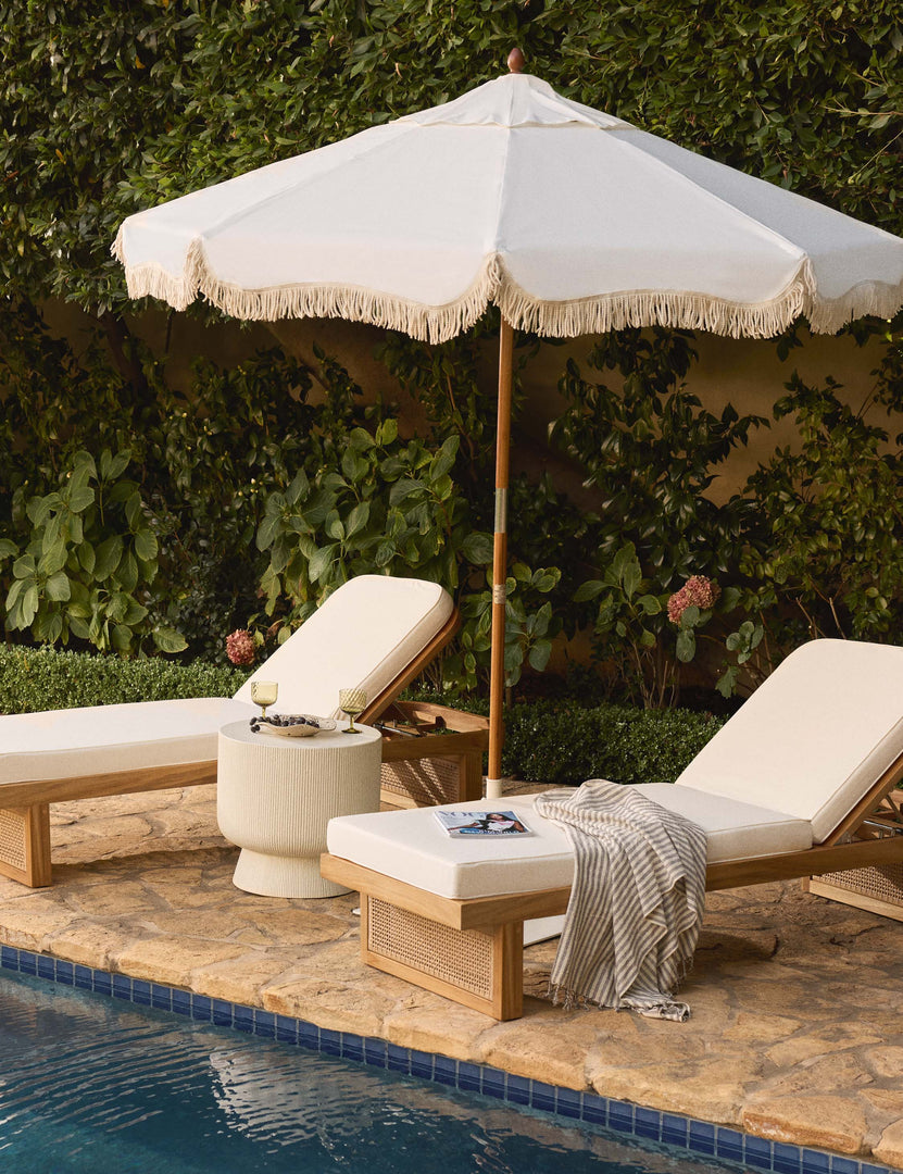#color::antique-white | The Market vintage white umbrella by business and pleasure co with a cotton fringe sits beside a pool between two white lounge chairs