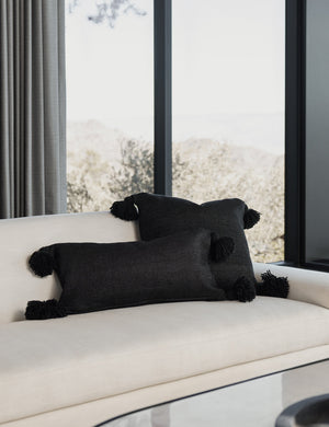 Sami black lumbar throw pillow with pom poms sits on a white linen couch