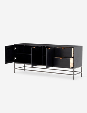 The three opened doors and two opened drawers of the Rosamonde black wood sideboard with brown leather pulls and a metal base