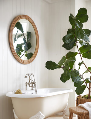 Marsali rattan framed round mirror hanging above a clawfoot bathtub