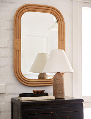 Marsali rattan framed wall mirror hanging above a cabinet styled with a table lamp and decorative tray