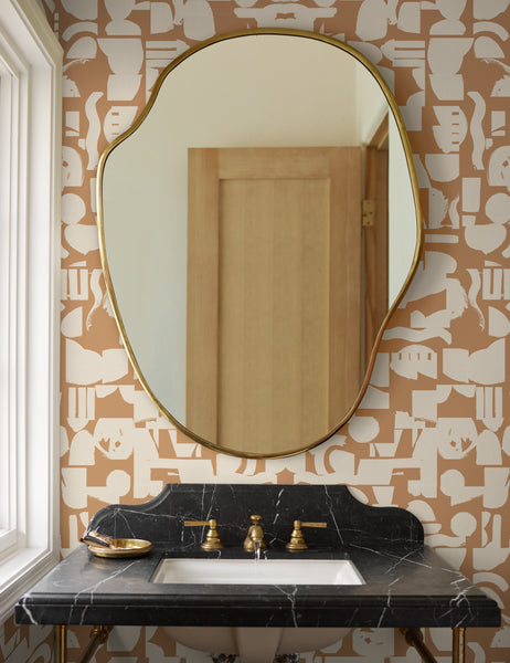 #size::small | The small puddle mirror hangs in a bathroom with abstract wallpaper above a black marble sink with gold hardware