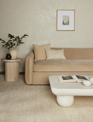The Taos ivory rug lays in a living room under a buff velvet sofa, a square coffee table, and a round side table