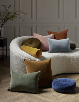 Charlotte velvet pillow in moss, rosewater, ice blue, burnt orange, and toast sit next to and on a cream boucle lounger