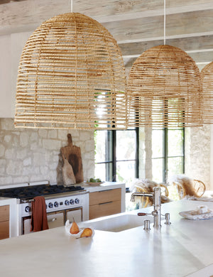 Three Beehive jute woven pendant lights are hung above a kitchen island in a kitchen with stone walls